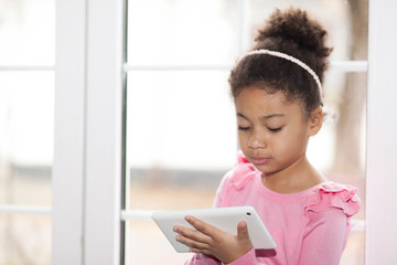 Adorable little african american girl uses a tablet. Gadget training