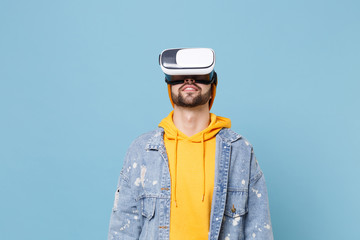 Young hipster guy in fashion jeans denim clothes posing isolated on pastel blue wall background studio portrait. People sincere emotions lifestyle concept. Mock up copy space. Watching in headset.