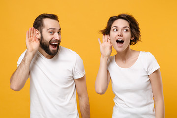 Curious young couple friends bearded guy girl in white empty t-shirts posing isolated on yellow...