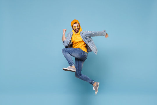 Side view of happy young hipster guy in fashion jeans denim clothes posing isolated on pastel blue background studio portrait. People lifestyle concept. Mock up copy space. Jump doing winner gesture.