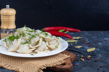 Boiled dumplings on a white plate. In the background is a wooden hodgepodge, greens, red peppers and bay leaves.