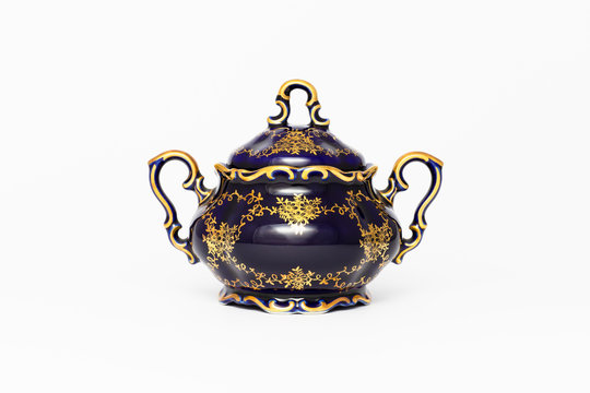Closeup of a beautiful cobalt blue colored vintage porcelain sugar bowl with golden floral pattern on white background