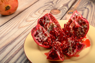 Ripe juicy pomegranate cut into several parts on a ceramic plate on a wooden background. Close up.