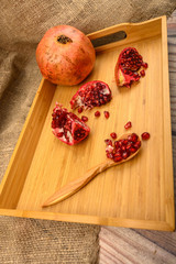 Ripe juicy pomegranate, pomegranate slices and pomegranate seeds in a wooden spoon on a wooden tray on a wooden background. Close up.
