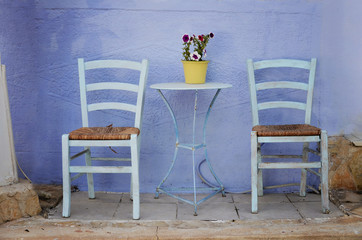 Fototapeta na wymiar Wooden two chairs and stylish table on the blue background wall in greek style. Outdoor patio cafe with empty sitting place.