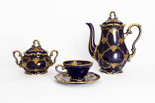 Closeup of a beautiful cobalt blue colored vintage porcelain tea set with golden floral pattern on white background. The set includes a tea pot, a sugar bowl and a tea cup.