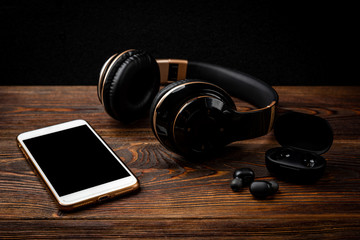 Black wireless headphones and mobile phone on dark wooden background.