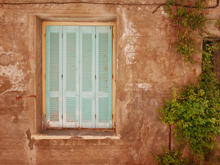 Fototapeta na wymiar Old closed window with blue wooden shutter in old house. Vintage and rural style of architecture. 