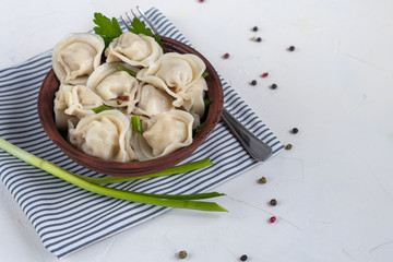 Boiled dumplings with feathers of green onions. In the background are greens, red peppers and bay leaves. In a transparent bowl sour cream.