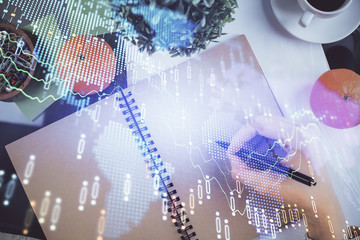 Forex chart hologram on hand taking notes background. Concept of analysis. Double exposure