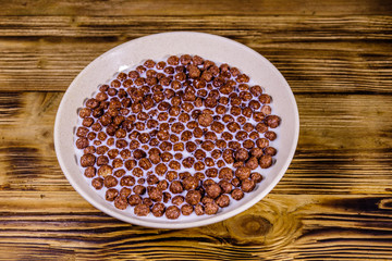 Ceramic plate with chocolate cereal balls in milk on wooden table