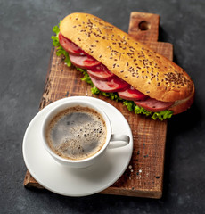 coffee and a large panini sandwich with sausage and cheese on a stone background