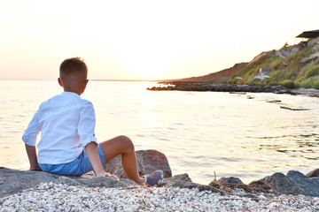 Fototapeta na wymiar Boy sitting on the seashore watching the sunset
