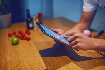 Obraz premium Close up of caucasian chef leaning on kitchen counter and searching for recipe on tablet.