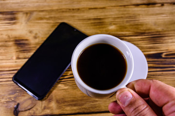 Fototapeta na wymiar Modern smartphone with blank screen on a wooden background and hand with cup of coffee