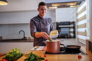 Young happy smiling caucasian chef in uniform putting pasta into pot with boiling water. Italian cuisine.