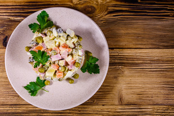 Ceramic plate with russian traditional new year salad olivier on a wooden table. Top view