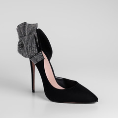 Womens black suede high heel shoes with a decorative bow element with shiny rhinestones on heel. Close-up side view. On a white background and natural shadows.
