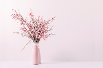 Fresh bouquet of pink flowers in vase on white shelf on pink wall background. Floral home decor.