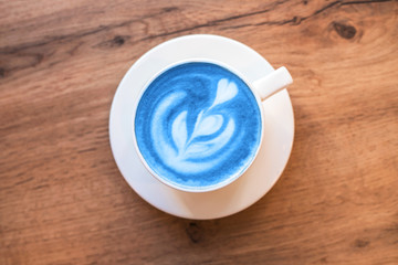 Fresh blue matcha with frothy foam, white coffee cup top view closeup on gray wooden background. Flat lay style.