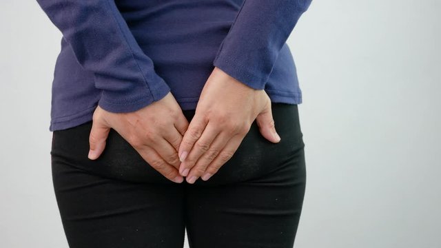Close up of woman hands touch at her buttom, suffering from hemorrhoids on grey background. Health care and medical concept.