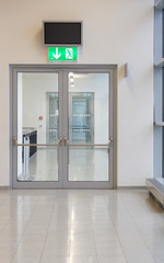 Double-leaf glass door with a green emergency exit lamp above it
