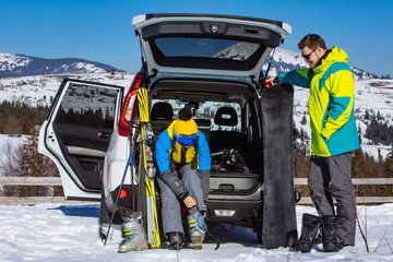 Fototapeta premium man and woman dressing into ski equipment near suv car