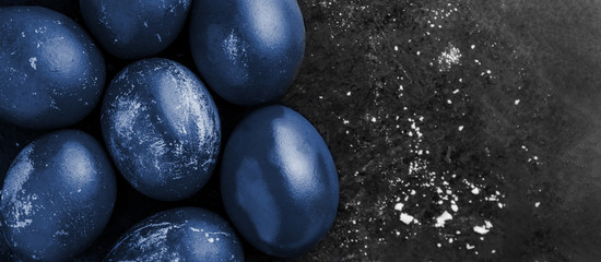 card with easter eggs painted in classic blue color shiny dye style on black background with crumbs, egg shell with white stains, scuffs, scratches. handmade painted eggs. Flat lay with copy space