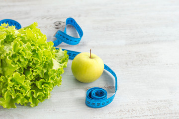 Green lettuce leaves and a green Apple on a light wooden background and a measuring tape.