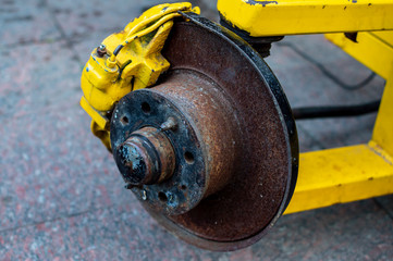 Old rusty brake disc on a yellow trailer frame.