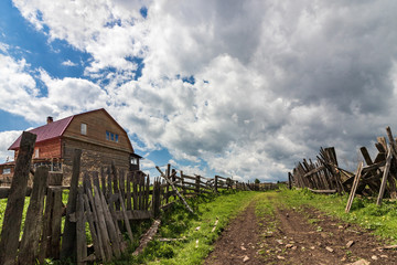 Village street, old wooden fence, blue sky with white clouds.