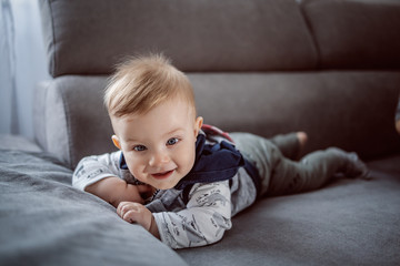 Cheerful happy little baby boy smiling and lying on stomach on couch in living room.