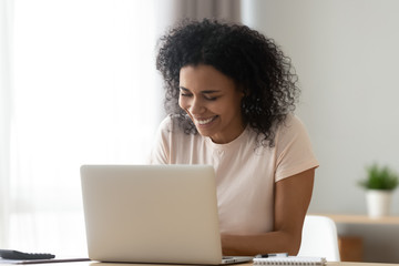 African woman sitting at desk laughing chatting with friend online