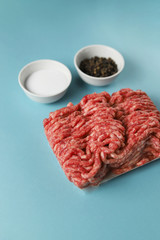 Raw ground beef, salt and black pepper on blue background. Food preparation concept, ingredients...