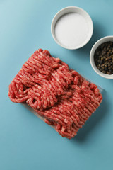 Raw ground beef, salt and black pepper on blue background. Food preparation concept, ingredients for burger, cutlet or meatball. Top view, flat lay