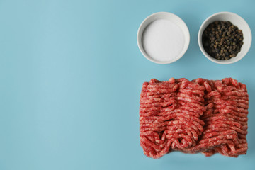 Raw ground beef, salt and black pepper isolated on blue background with copy space. Food preparation concept, ingredients for burger, cutlet or meatball. Top view, flat lay