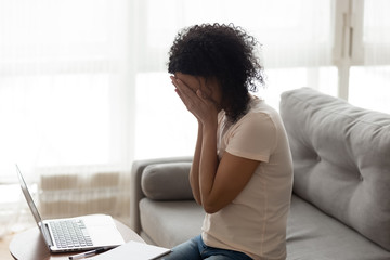 African woman sitting near computer cover face with hands crying