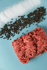 Raw ground beef, salt and black pepper on blue background. Food preparation concept, ingredients...
