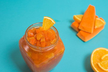 fresh nutritious orange jam with pumpkin slices and orange slices, healthy Breakfast with proper nutrition. jam in a glass jar on a blue background . space for text