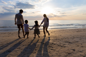 Happy Asian Family On Summer Vacation Father, mother, son and daughter holding hands Running down to the seashore together. Background sunset in sea. Relax Holiday and Travel concept.