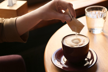 Woman adding sugar to aromatic coffee at table in cafe, closeup