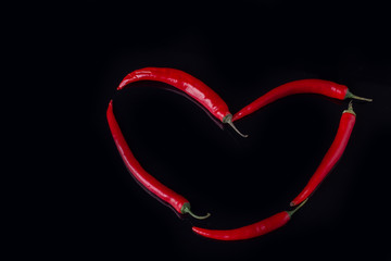 Heart shape made of hot chili peppers. Heart made with red chili peppers on black background.