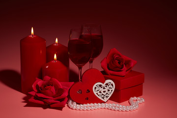 Gift boxes, two glasses with wine, burning candles, red roses and hearts on red background. Valentine's day. Wedding day.