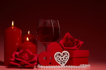 Gift boxes, two glasses with wine, burning candles, red roses and hearts on red background. Valentine's day. Wedding day.