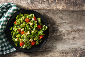 Salad with avocado, lettuce, tomato and flax seeds on wooden table. Top view. Copy space	
