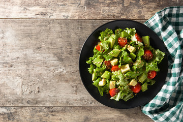 Salad with avocado, lettuce, tomato and flax seeds on wooden table. Top view. Copy space	