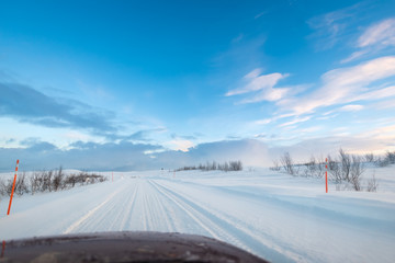 Road trip in the Arctic on a snow covered ice road with car hood / bonnet visible at the bottom of the frame