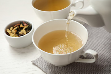 Pouring green tea into cup on white wooden table