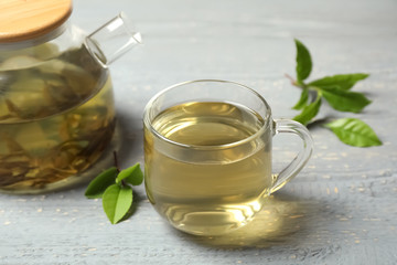 Cup of green tea, pot and leaves on grey wooden table