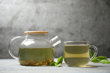 Cup of green tea, pot and leaves on grey wooden table